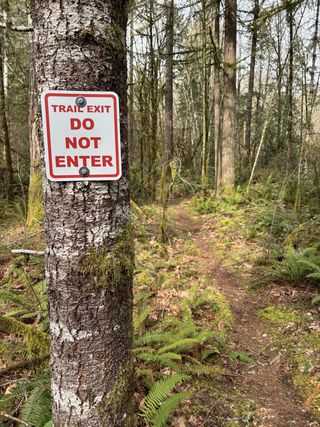 A sign posted on a trailside tree reads "Trail Exit. Do Not Enter."